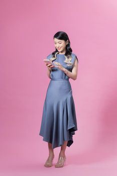 Pretty woman holding smartphone and browsing internet or chatting isolated over pink background in studio