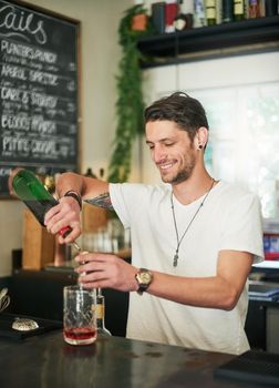 Making it look easy. a happy young bartender mixing a cocktail while standing behind the bar.