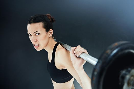 I will prove no goal is out of reach. a young woman lifting weights against a dark background.