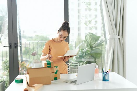 woman checking purchase order in laptop and write in the delivery on package box sell online 
