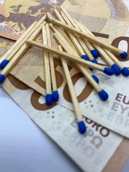 Closeup of several matchsticks on euro banknotes with selective focus on foreground