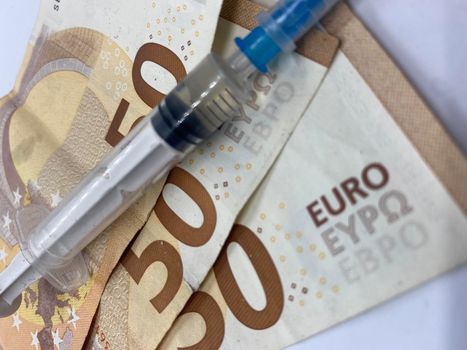 Closeup of a syringe with needle on euro banknotes with selective focus on foreground