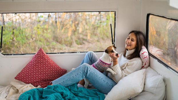 Caucasian woman sitting in a van hugging with dog Jack Russell Terrier. Travel in a camper in the fall.