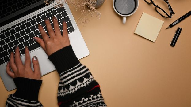 Young female in warm sweater typing on keyboard of laptop computer.