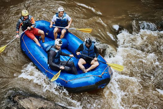 Here comes the next rapid. High angle shot of a group of determined young men on a rubber boat busy paddling on strong river rapids outside during the day.