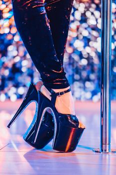 Legs in high sexy shoes near pylone. Striptease dancer moving on stage in strip night club. Pole dancing background.