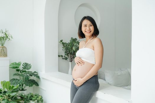 joyful pregnant woman with hands on belly posing at camera