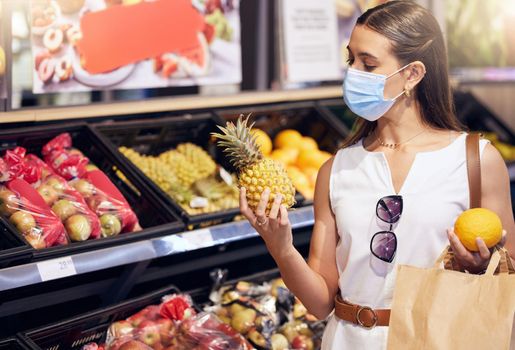 Woman grocery shopping while wearing a mask for medical protection against covid in a supermarket. Young female buying healthy, organic and wellness fruit consumables at a food store.