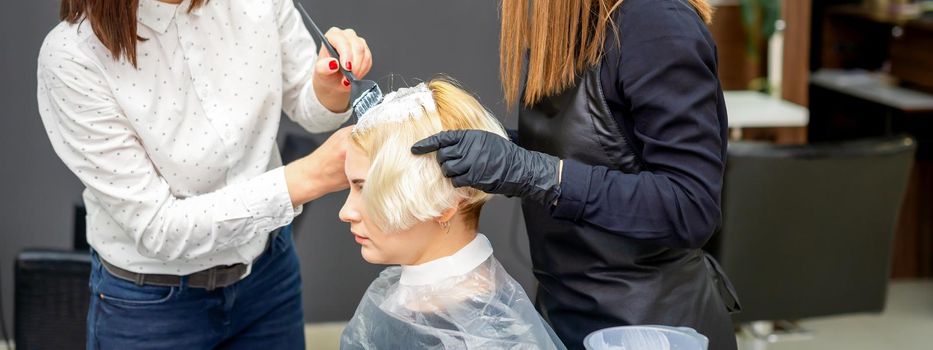 Two hairdressers dyeing hair of woman