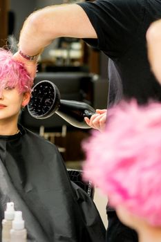 Hairdresser drying pink hair of client