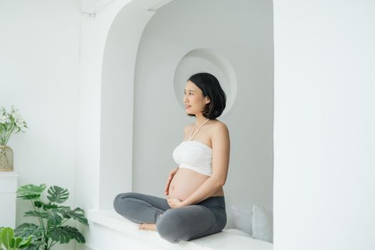 Pregnant Chinese Asian female sitting cross legged in living room