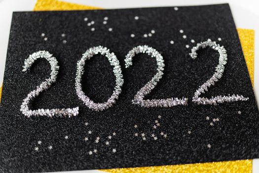 The year 2022 is written in New Year's silver tinsel on a black background along with silver stars. Greeting card.