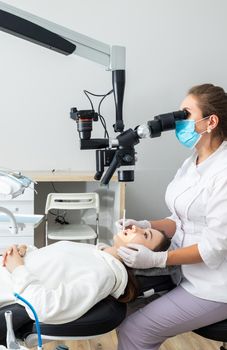 Female dentist using dental microscope treating patient teeth at dental clinic office. Medicine, dentistry and health care concept. Dental equipment