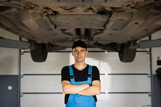 Mechanic man standing in front of the garage. Joyful young bearded man motor mechanic in overalls standing in workshop. Motor mechanic. Concept of small business, own business