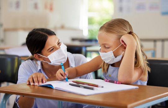 Education, covid and learning with face mask on girl doing school work in classroom, teacher helping student while writing in class. Elementary child wearing protection to stop the spread of a virus