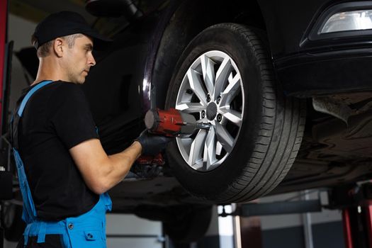 Car mechanic replacing car wheel of lifted automobile at repair service station. Assembly or dismantling of the wheels in the workshop. repair and maintenance of the car in service