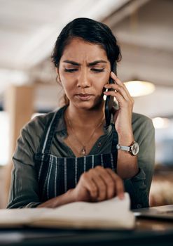 Young and confused business owner on the phone making a stock order for her cafe, restaurant or coffee shop. A female employee, manager or store owner looking at a book of products or inventory.