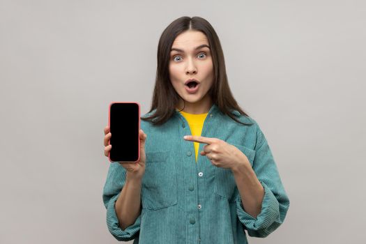 Surprised happy woman showing phone with empty screen, pointing cell phone with space foe promotion.