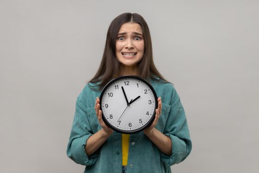 Unhappy woman holding big clock and looking displeased irritated, showing wall watches to hurry up.