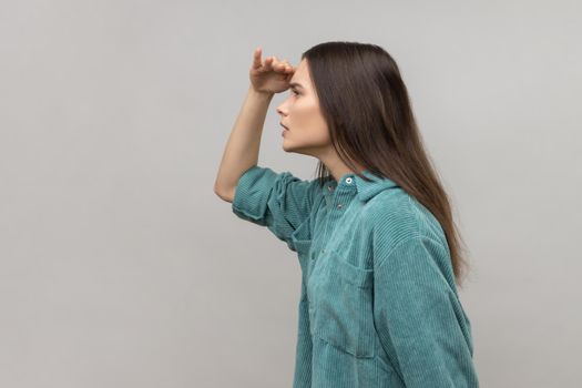 Woman keeping palm over head looking attentively far away, peering with expectation at long distance