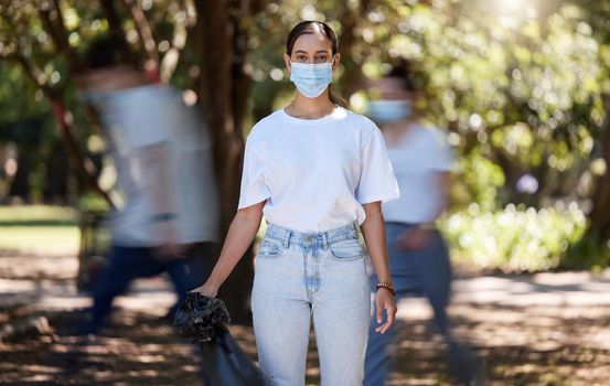 Woman in covid face mask cleaning the park for clean, hygiene and safe green environment. Responsible activist, volunteer or community service worker with rubbish, trash and garbage in a plastic bag