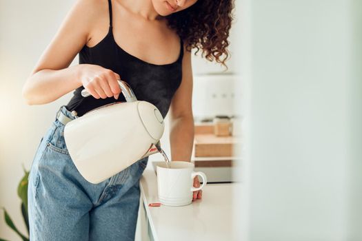 Woman making a cup of tea for breakfast before starting her morning at home. Female trying a health cleanse with organic green tea, beginning a slimming detox or diet with a healthy drink