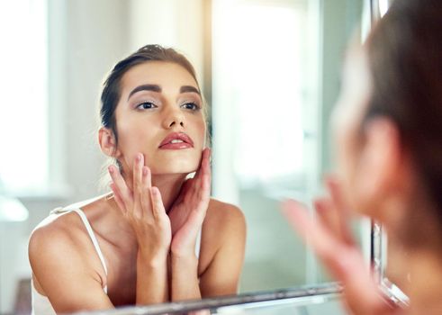 Keeping her skin in fabulous condition. an attractive young woman inspecting her skin in the mirror.