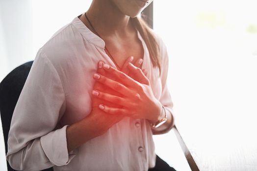 Stress is a high factor in causing chest pain. Closeup shot of an unidentifiable businesswoman holding her chest in pain.