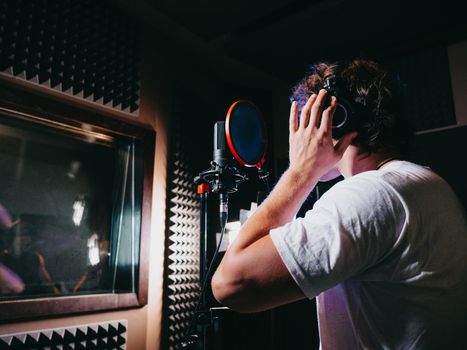 Young handsome singer man puts on headphones in the studio. Recording new melody or album. Male vocal artist with curly hair preparing for working