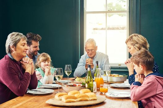 We are thankful to have each other. a peaceful family seated around the dinner table and saying grace with eyes closed at home.