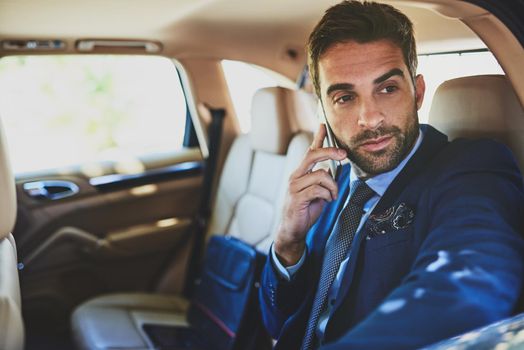 Making business calls on the go. a confident young businessman talking on his cellphone while being seated in the back of a car.