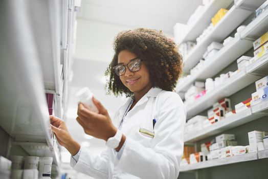 Always read the label. a cheerful young female pharmacist reading the label of a medication bottle inside of a pharmacy.