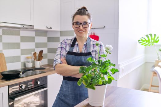 Portrait of housewife woman with potted flower plant at home kitchen