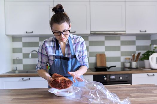 Woman packs pork leg marinated with spices in baking sleeve