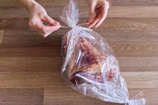 Hands woman packs pork leg marinated with spices in baking sleeve