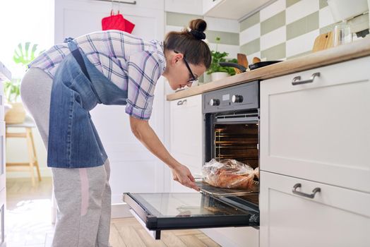 Woman preparing pork in baking sleeve at home, puts tray of meat in oven