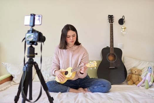Teenager girl plays music on ukulele, online learning and chatting with followers
