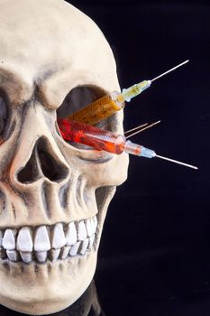 Humans skull with colorful syringes in the eye hole.
