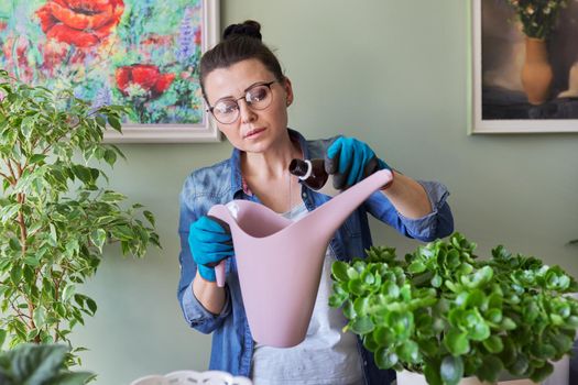 Woman pours liquid mineral fertilizer, in watering can with water