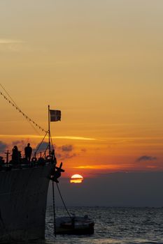 Old moored Greek warship with flag against sea level sunset.