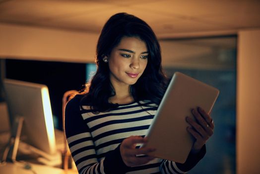 Making every effort to stay ahead of her deadlines. a young businesswoman working late on a digital tablet in an office.