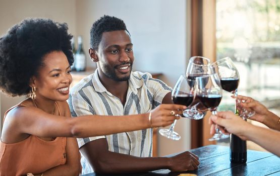 Black couple celebrating their anniversary with friends, toasting and drinking red wine. Happy girlfriend and boyfriend bonding at a family gathering, together for an engagement or proposal