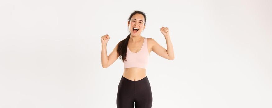 Sport, wellbeing and active lifestyle concept. Empowered and strong asian female athlete, fitness girl encourage herself for good workout, fist pump and shouting supportive, gaining goal