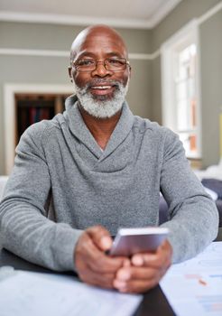 This banking app is wonderful. Cropped portrait of a senior man using his cellphone while working on his finances at home.