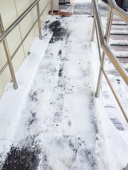 Modern ramp with metal railings for accessible movement of people with disabilities, ramp covered with snow, vertical photo