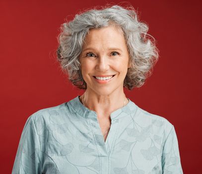 . Portrait of senior, happy and cheerful woman standing against a red studio background. Mature woman with healthy, white and clean teeth showing oral and dental health with a friendly bright smile.