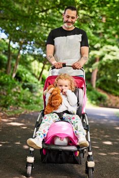 Daddy and daughter time. Portrait of a father pushing his little daughter in a stroller outdoors.