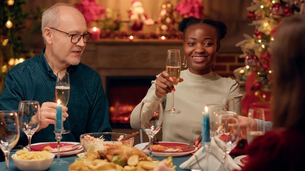 Laughing heartily diverse people clinking champagne glasses while enjoying Christmas dinner