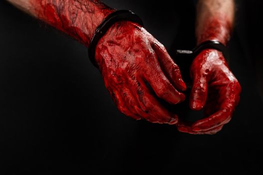 Close-up of male bloody handcuffed hands on a black background.