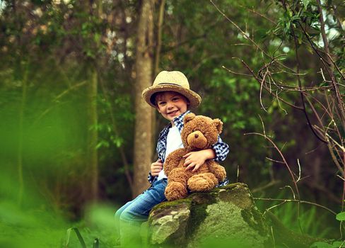 Teddy is quite happy when were outdoors. a little boy sitting in the forest with his teddy bear.